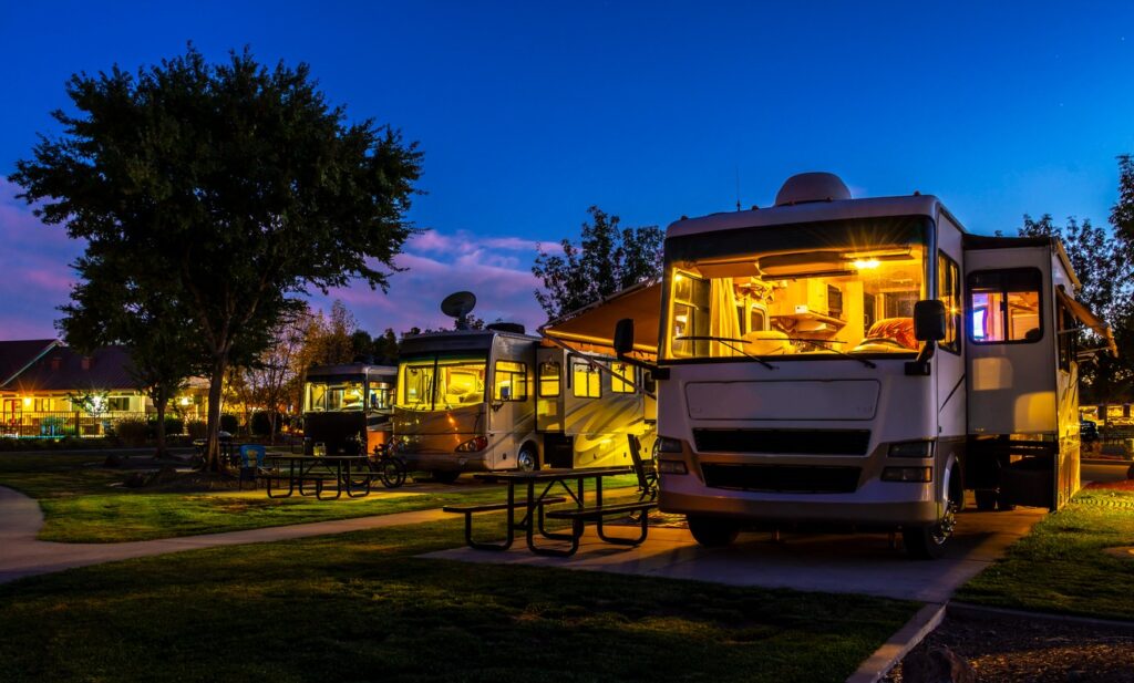 A row of RVs parked in an RV park with their internal lights on at night.